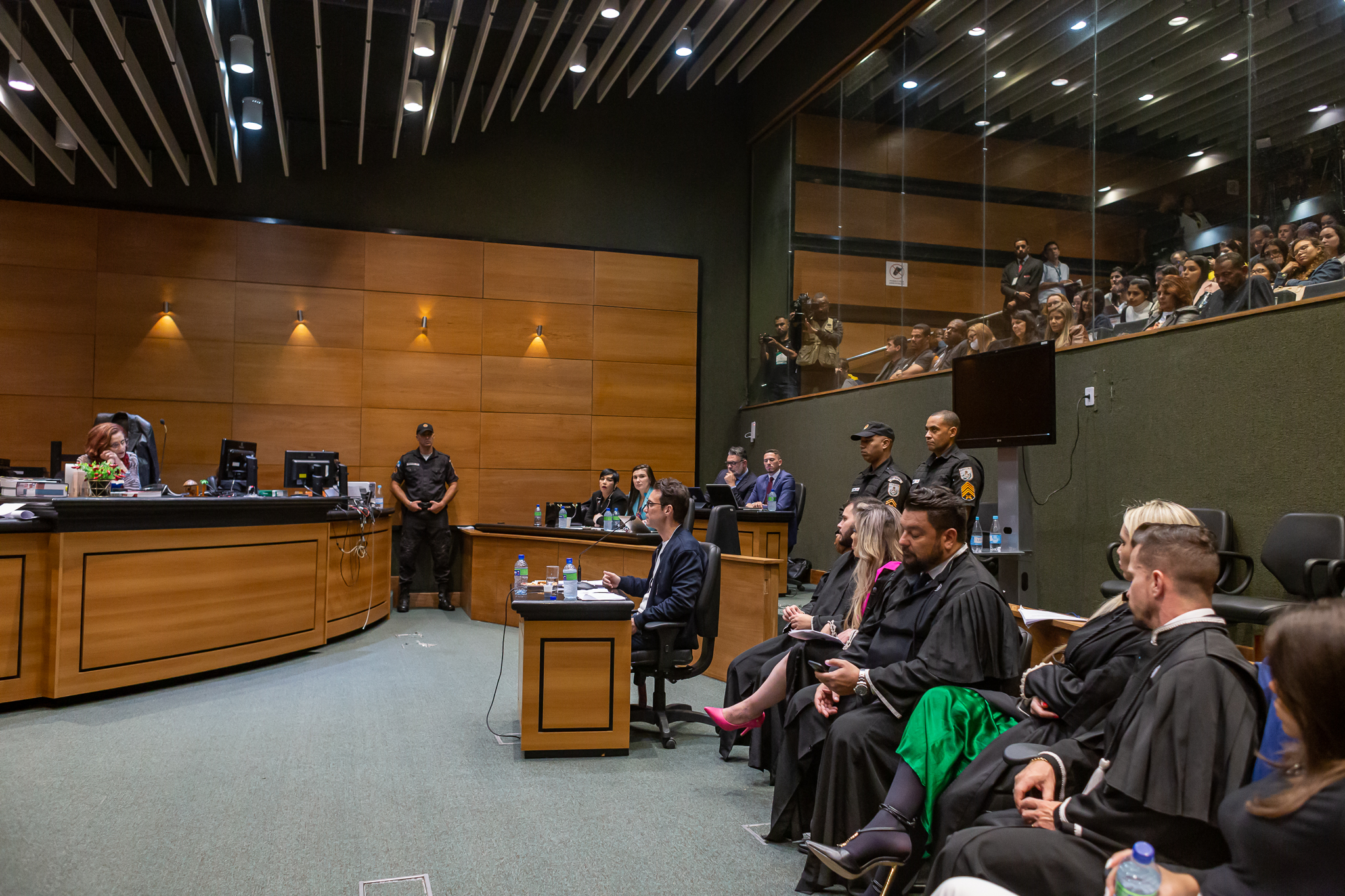 No plenário do Segundo Tribunal do Júri, Jairinho está sentado no banco destinado ao réu olhando para a juíza Elizabeth Louro, que está sentada à frente dele. Os advogados de defesa de Jairinho estão sentados ao seu lado esquerdo.