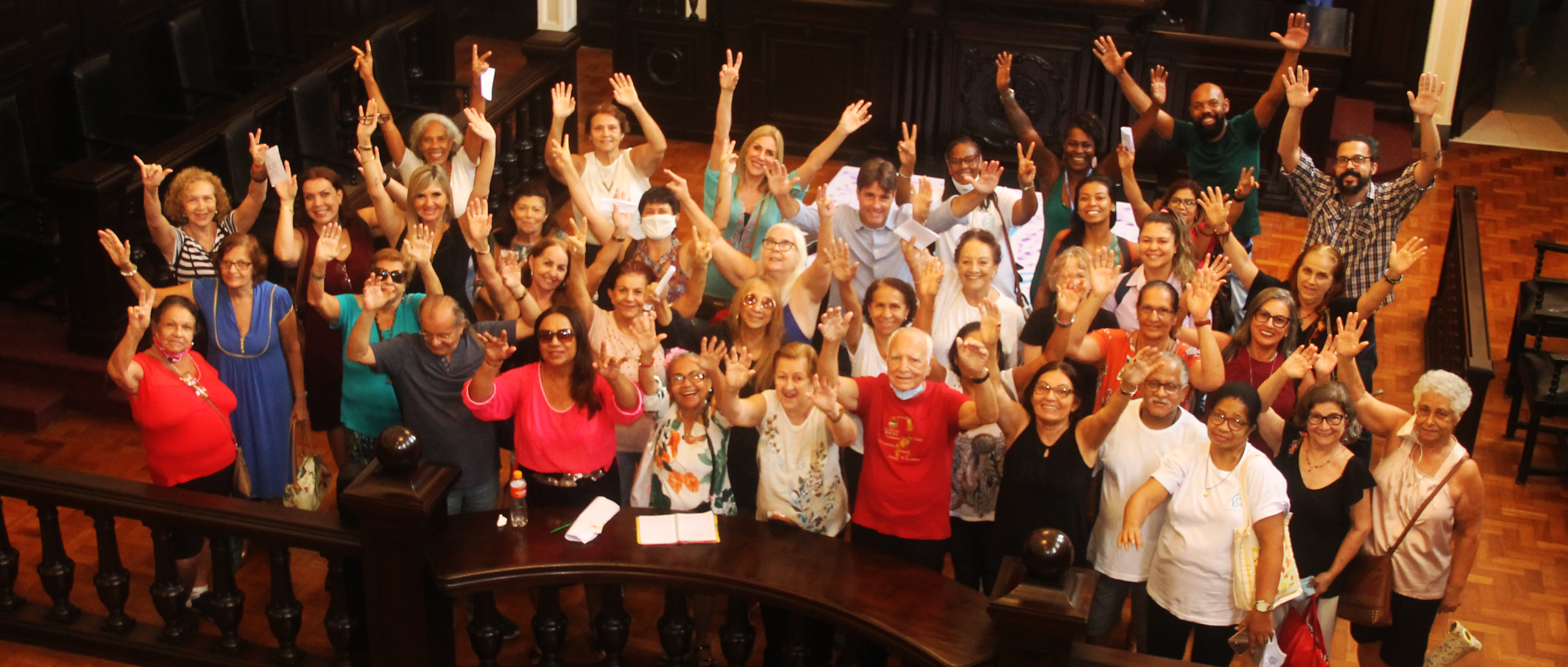 Grupo de participantes do lançamento do II Concurso de Poesia Palavra Viva se reúnem no Museu da Justiça com os braços para o alto 