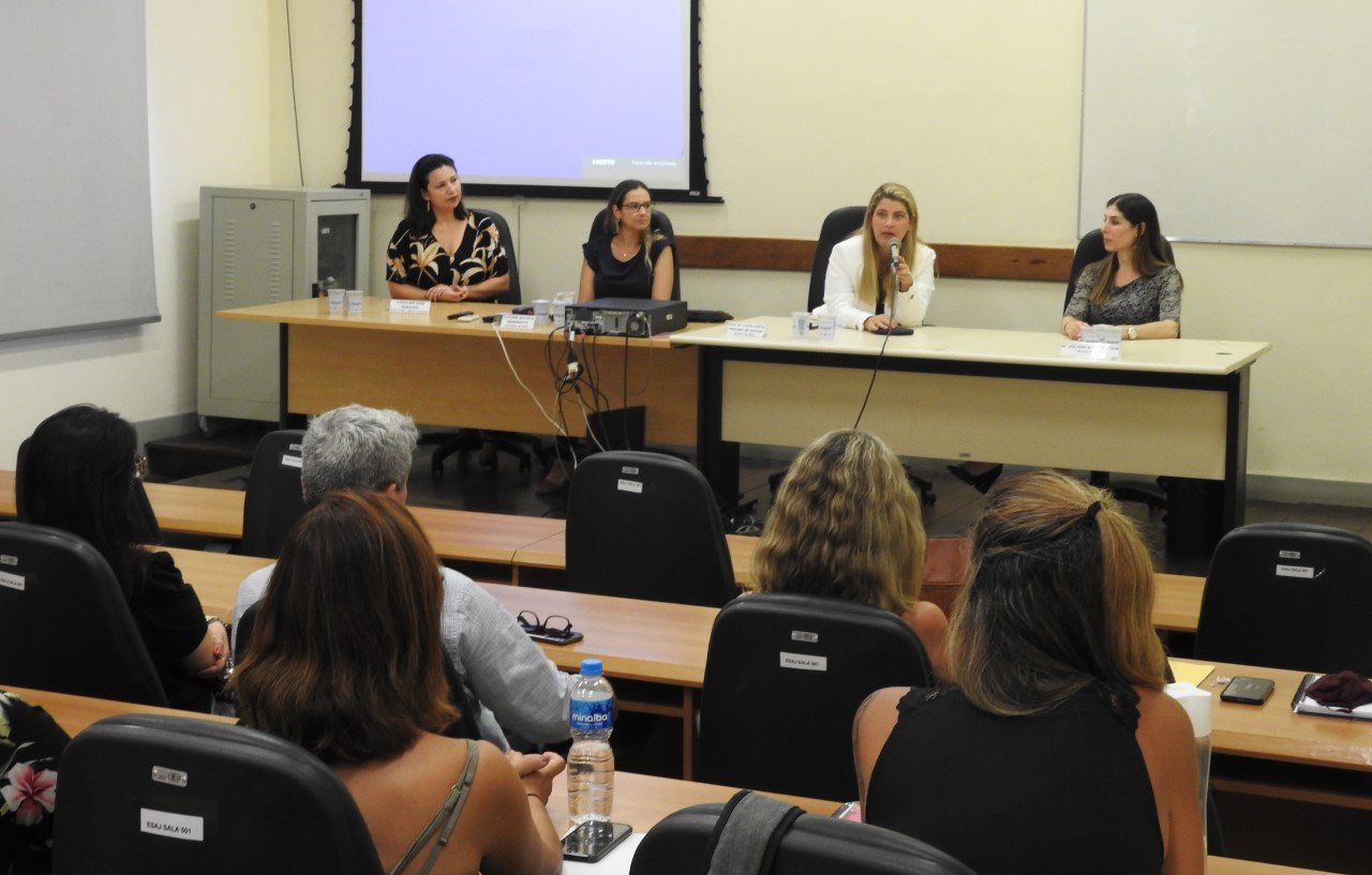 Imagem da mesa com plateia de costas. Na mesa, da direita para esquerda: Juliana Dias Badajós da ouvidoria, Luciene Batista Marequito, instrutora ESAJ, Lúcia Frota, diretora ESAJ com a juíza Juliana Kalichsztein.