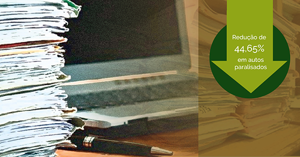 Imagem de processos e de um computador em cima de uma mesa e por cima de ssas imagens aparece uma seta para baixo dentro de um circulo indicando a redução da meta