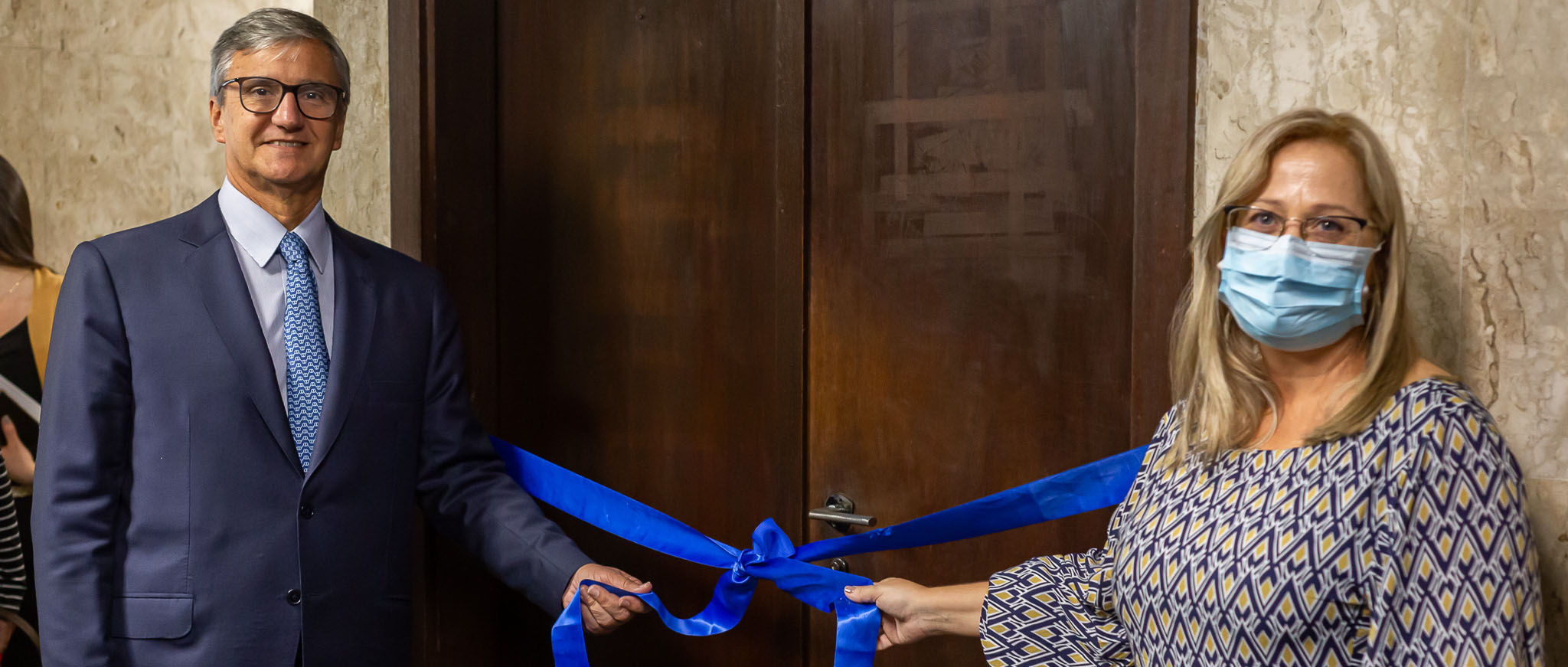 O presidente do TJRJ, desembargador Henrique Figueira, e a juíza Gisele Guida seguram faixa azul com laço de inauguração em frente à porta da nova vara