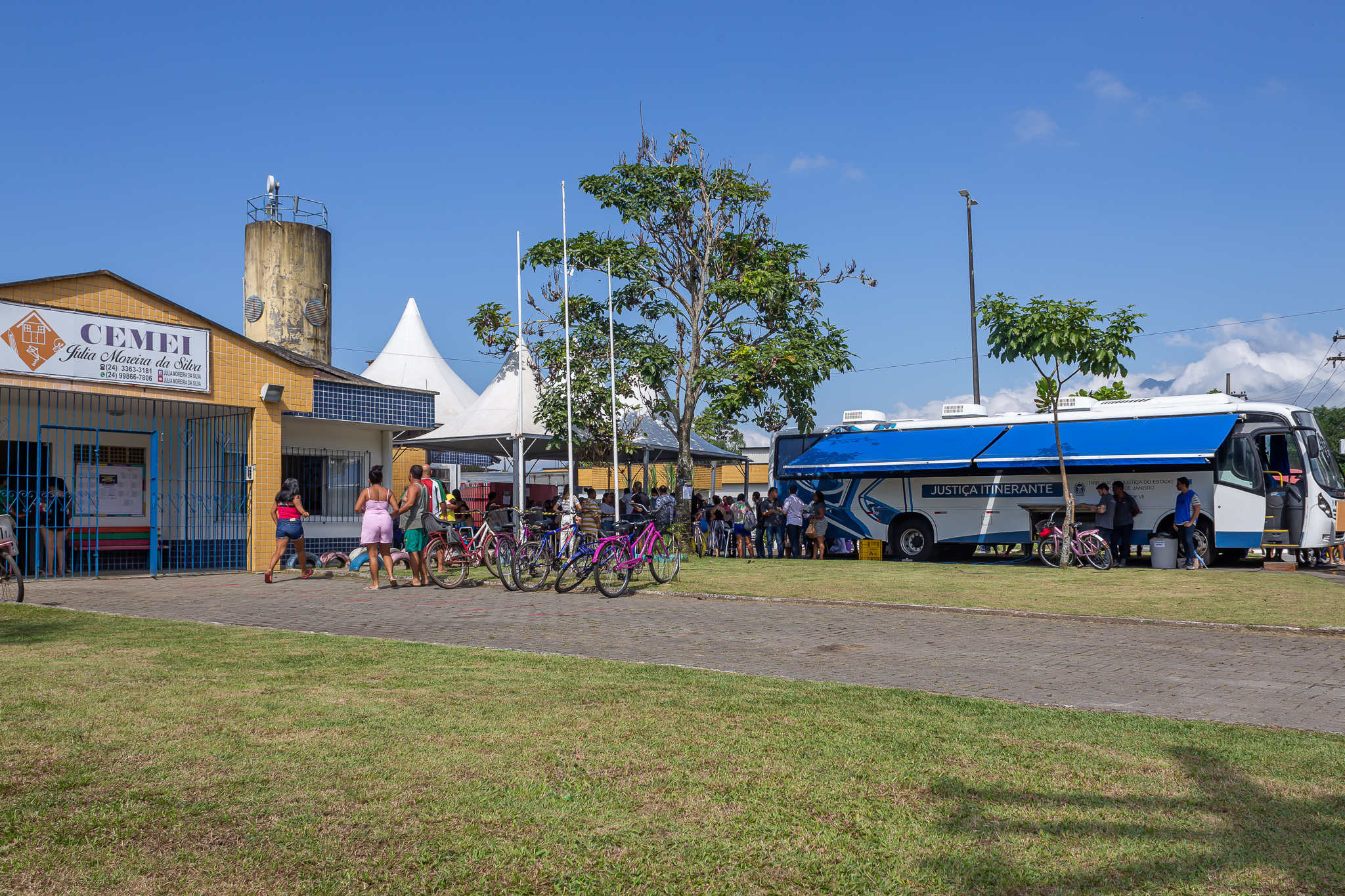 Imagem colorida. Fachada amarela de uma escola, um gramado verde e ao lado esquerdo o ônibus da Justiça Itinerante