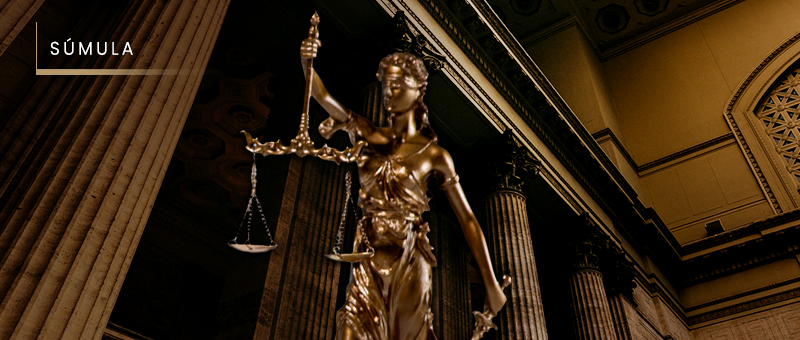 Legenda:#ParaTodosVerem: Acima, no canto esquerdo, o título “SÚMULA”. Imagem de salão de tribunal, em tom cobreado, com diversas colunas cilíndricas, e, em primeiro plano e tamanho natural, a escultura da deusa Têmis – a deusa da Justiça.