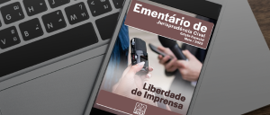 Celular sobre um teclado de Notebook.  A tela do celular exibe a capa da edição especial do Ementário de Jurisprudência Cível sobre Liberdade de Imprensa, com uma foto de duas pessoas, uma segurando um pequeno gravador e a outra segurando em uma das mãos um microfone e na outra um celular.  A logo do PJERJ aparece centralizada na parte inferior da capa.