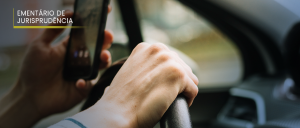 #ParaTodosVerem: No canto superior direito, o texto “EMENTÁRIO DE JURISPRUDÊNCIA”. Fundo levemente desfocado do interior de um carro, mais precisamente na posição do motorista, aparecendo as mãos do próprio: a esquerda, segurando o celular; a direita, segurando o volante.