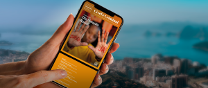 #ParaTodosVerem: Mão de mulher branca segurando um celular, cujo display apresenta a capa do EMENTÁRIO DE JURISPRUDÊNCIA CÍVEL E CRIMINAL – NOVEMBRO/2023, edição especial: DISCRIMINAÇÃO RACIAL. Criança preta, de camisa de manga comprida mostarda, tendo as mãos espalmadas à frente e nelas o seguinte protesto: BASTA JÁ! Ao fundo, a cidade do Rio de Janeiro.