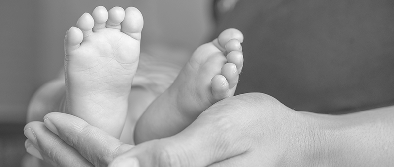 Pés de um bebê apoiados por mão de uma pessoa adulta