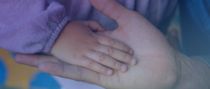 Palma da mão estendida de uma pessoa adulta, tendo por sobre ela a palma da mão estendida de uma criança