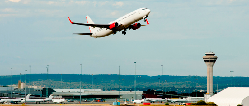 Imagem de avião decolando de aeroporto. Ao fundo aparece um aeroporto e a torre de controle das aeronaves