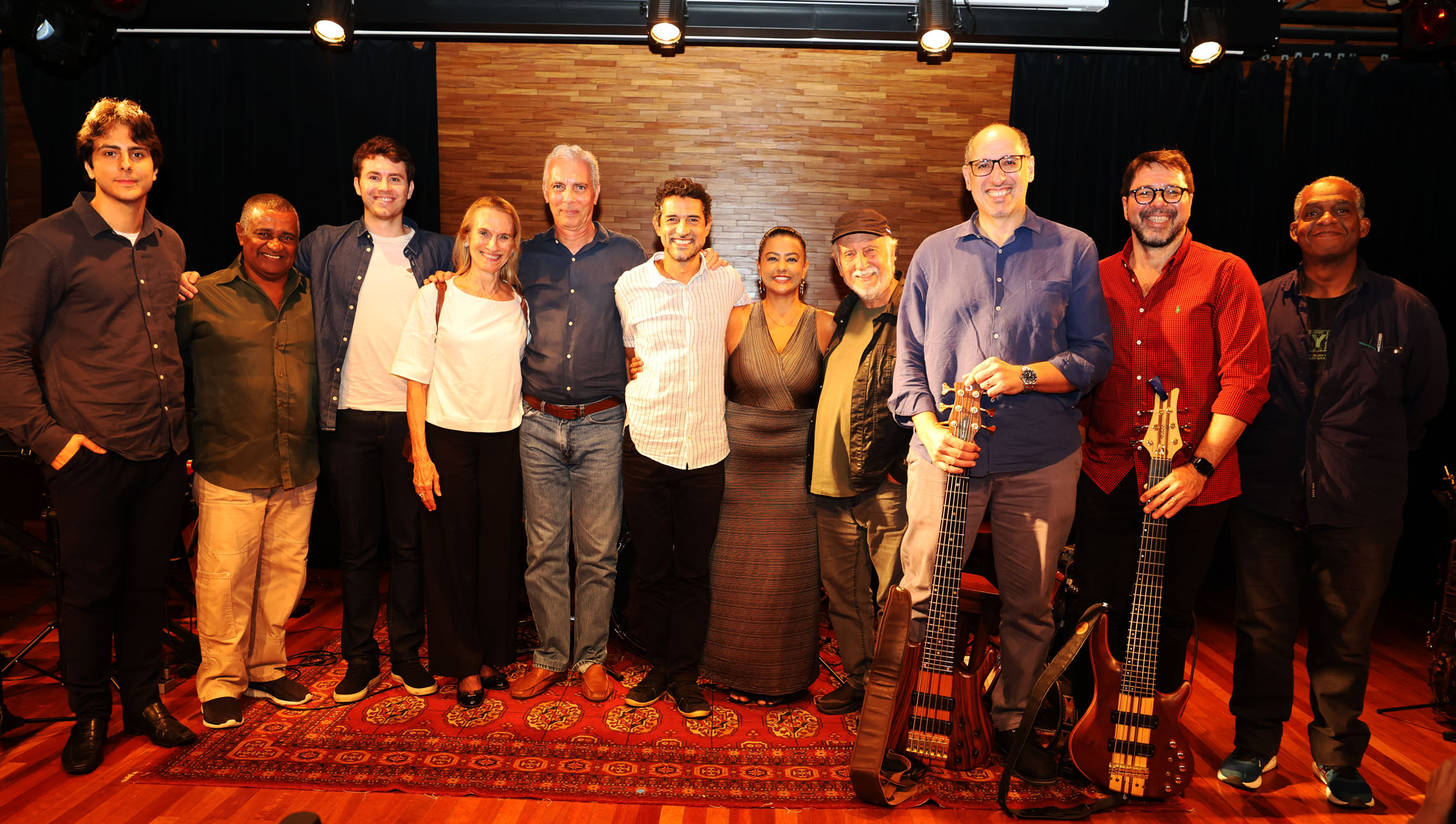 A imagem mostra a banda com a desembargadora Cristina Gaulia e o músico Roberto Menescal no palco da Sala Multiuso