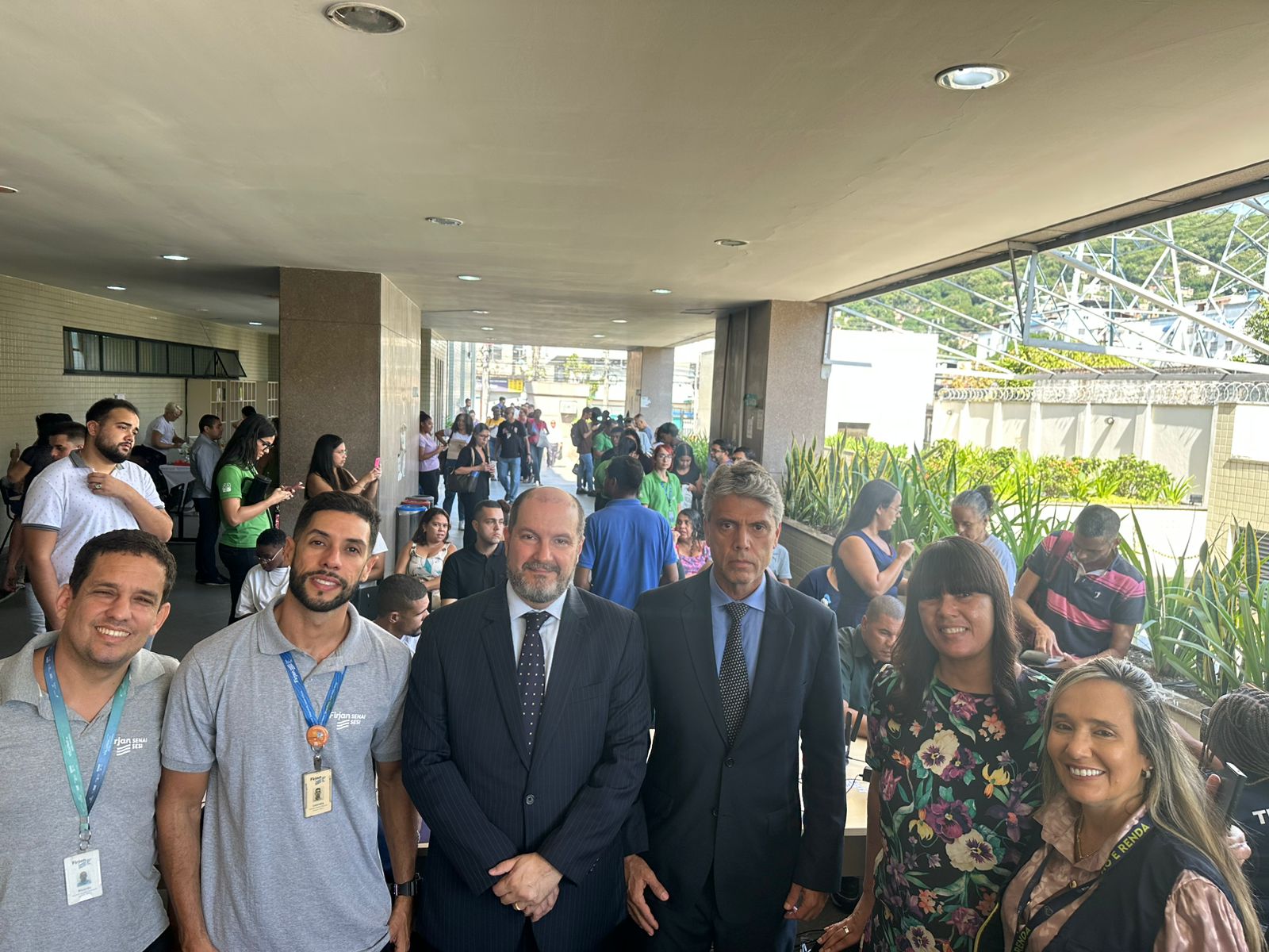 A imagem mostra muitas pessoas circulando ao fundo e seis pessoas posando para a foto na frente em ação realizada no Fórum Regional de Madureira