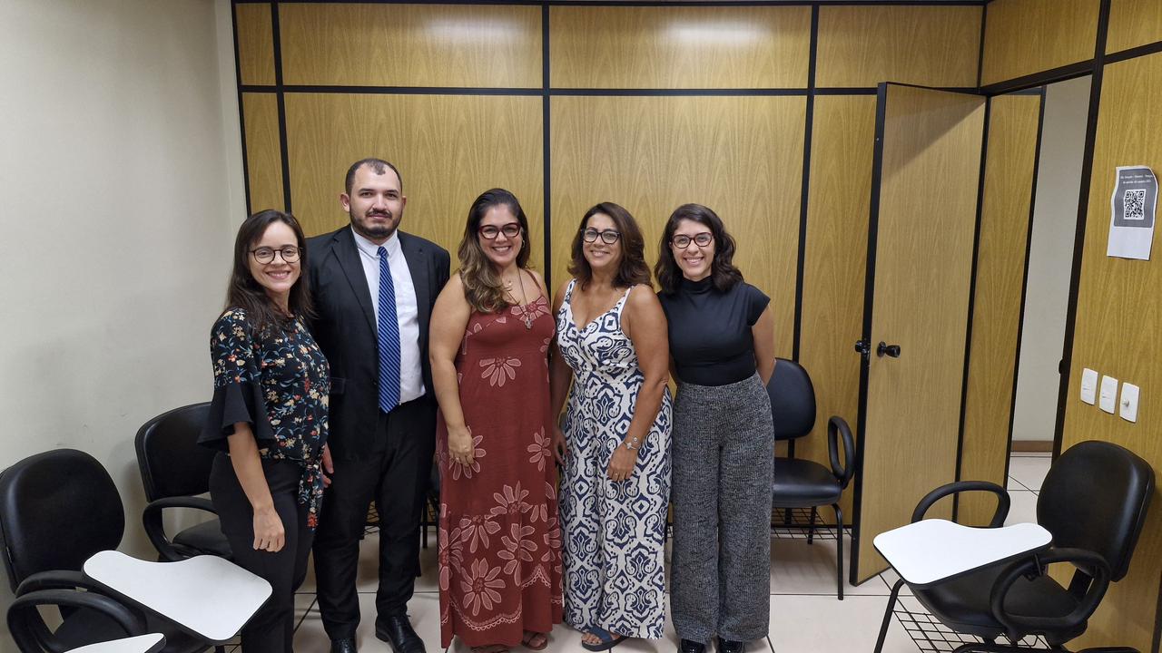 A imagem mostra quatro mulheres e um homem posando para a foto em uma sala.