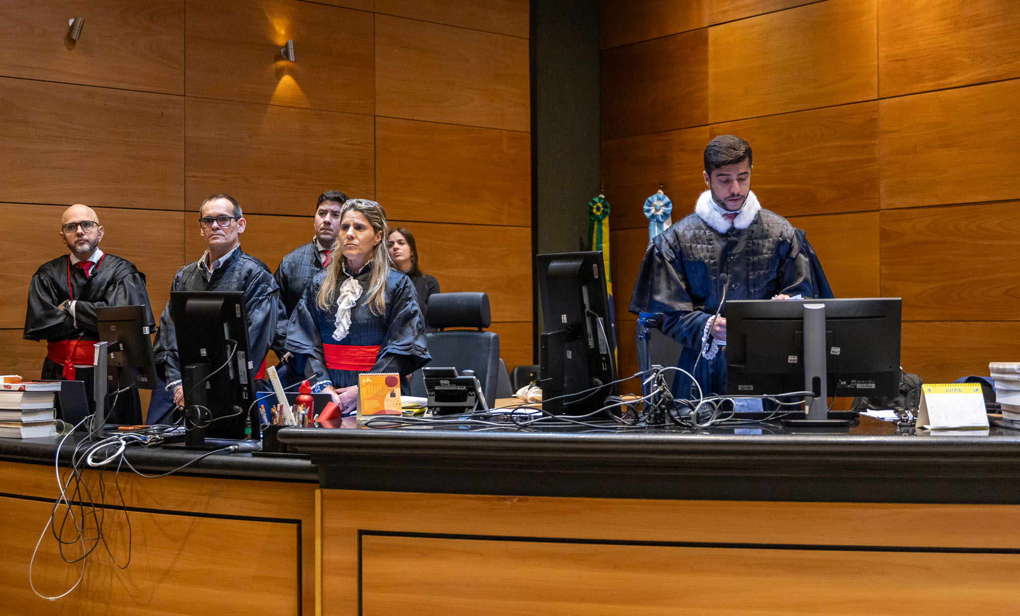 Foto do plenário com os promotores à esquerda e o juiz ao centro lendo um papel