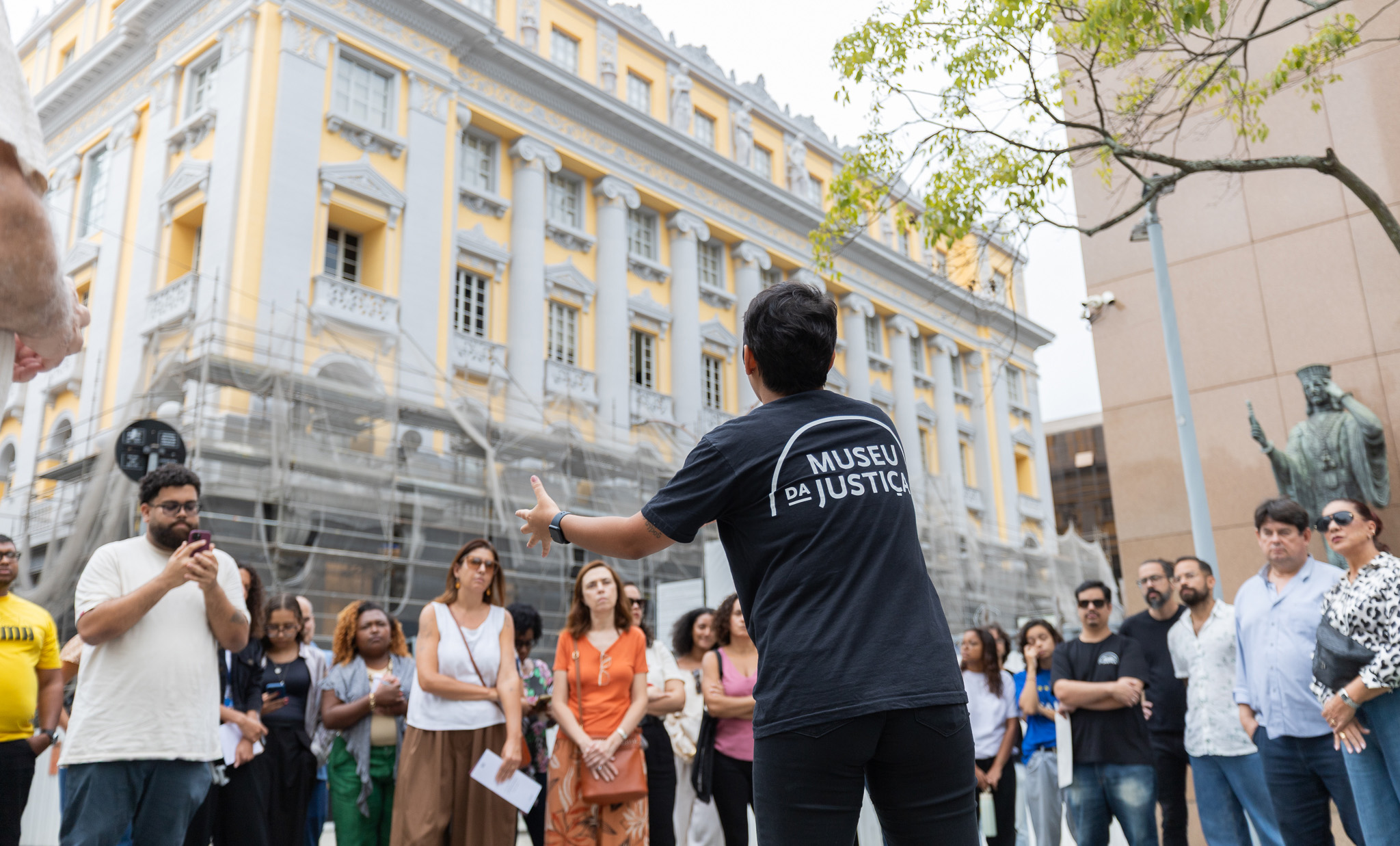 O grupo de visitantes ouve as informações do guia em frente ao Museu da Justiça 
