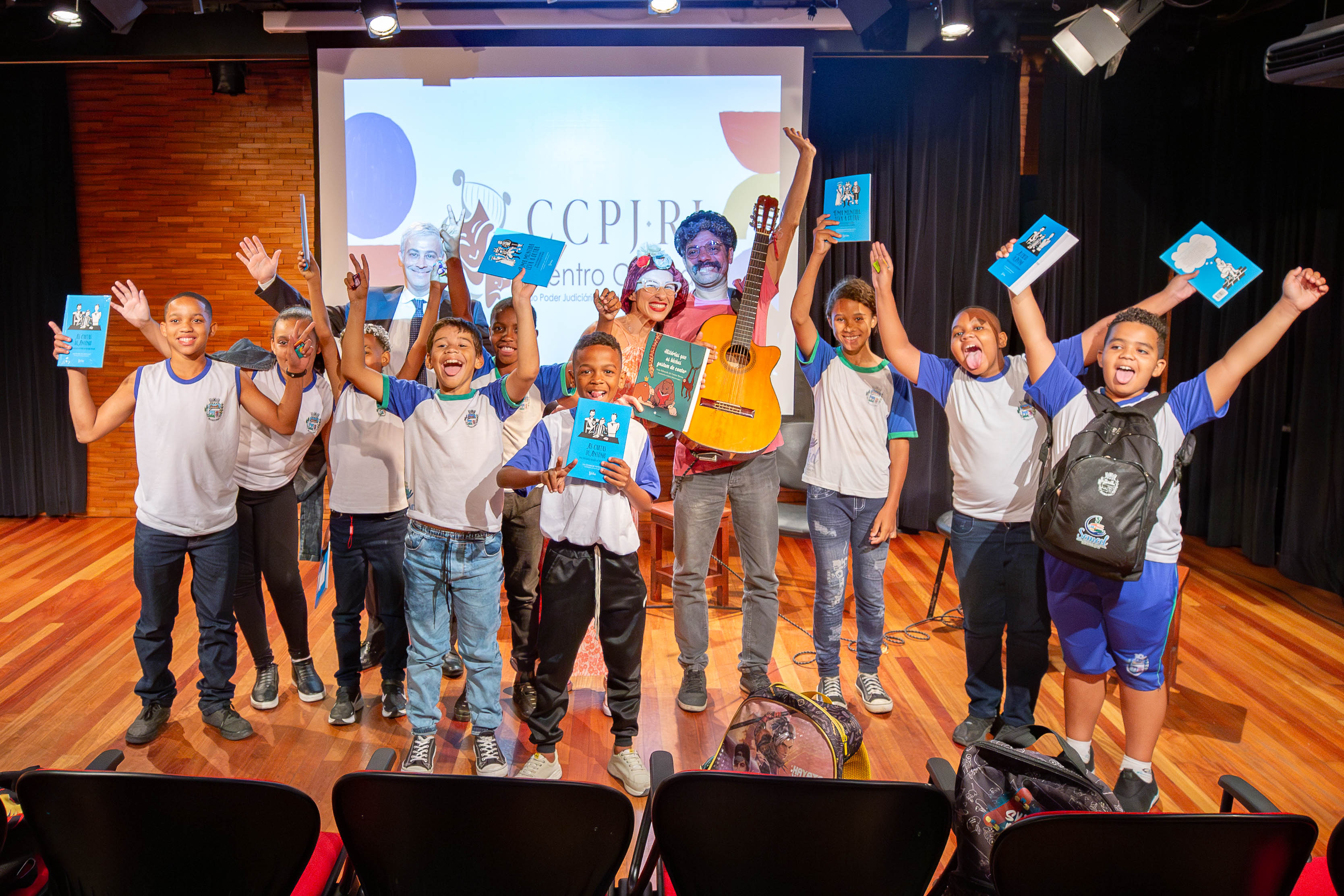 Grupo de crianças, juiz, professora e músico posam para foto no palco da Sala Multiuso 