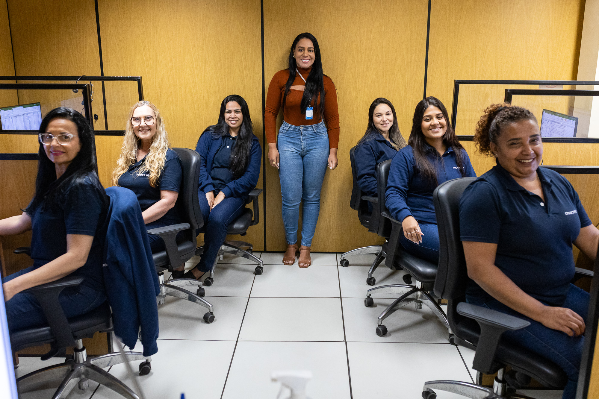 Foto mostra telefonistas sentadas com a chefe do setor de pé em sala de atendimento