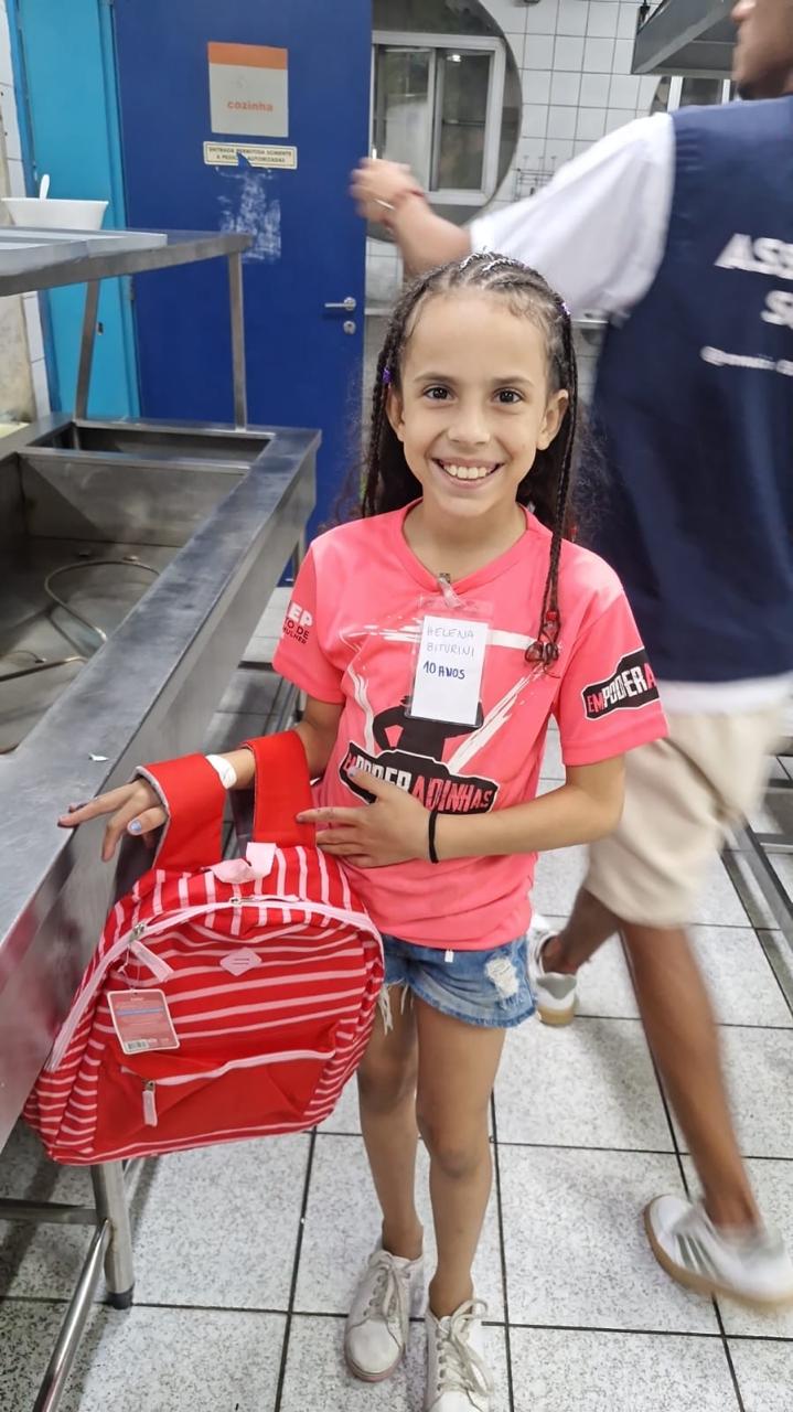 Menina posa para foto sorrindo e com a mochila vermelha que ganhou de presente