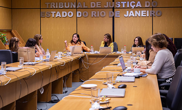 A imagem mostra uma mesa de reunião com cerca de dez mulheres conversando, incluindo a deputada federal Soraya Santos e a desembargadora Adriana Ramos de Mello. 