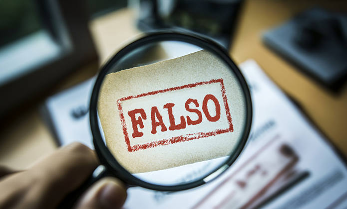 #ParaTodosVerem: Uma lupa em primeiro plano amplia a palavra “FALSO”, escrita em letras maiúsculas vermelhas dentro de um retângulo, sobre um pedaço de papel bege. Ao fundo, há documentos desfocados sobre uma mesa.