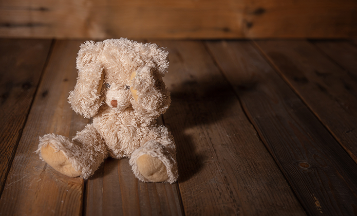 #ParaTodosVerem: Imagem mostra um urso de pelúcia sentado sozinho sobre um piso de madeira, em ambiente com luz suave.