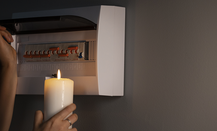 #ParaTodosVerem: Imagem mostra pessoa segurando uma vela acesa próxima a quadro de disjuntores aberto, instalado em parede interna.