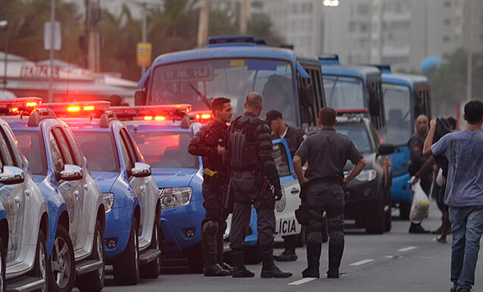 #ParaTodosVerem: Imagem mostra policiais e viaturas com luzes vermelhas ligadas numa rua, ao lado de ônibus e pessoas, sugerindo operação policial.